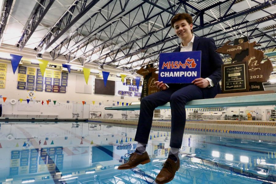 Charley+Bayer+%E2%80%9822+sits+on+the+diving+board+with+the+state+championship+trophies%2C+his+Division+3+Diver+of+the+Year+award%2C+and+his+MHSAA+Champion+Placard